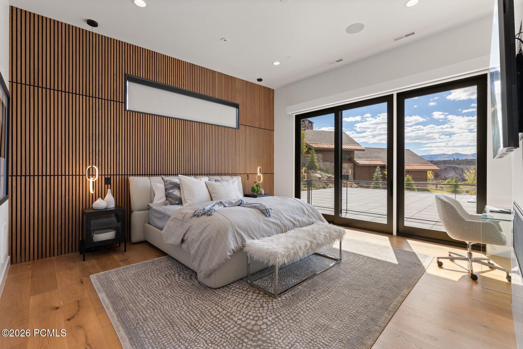 Modern bedroom with a wood-slat accent wall and deck doors overlooking distant mountains.