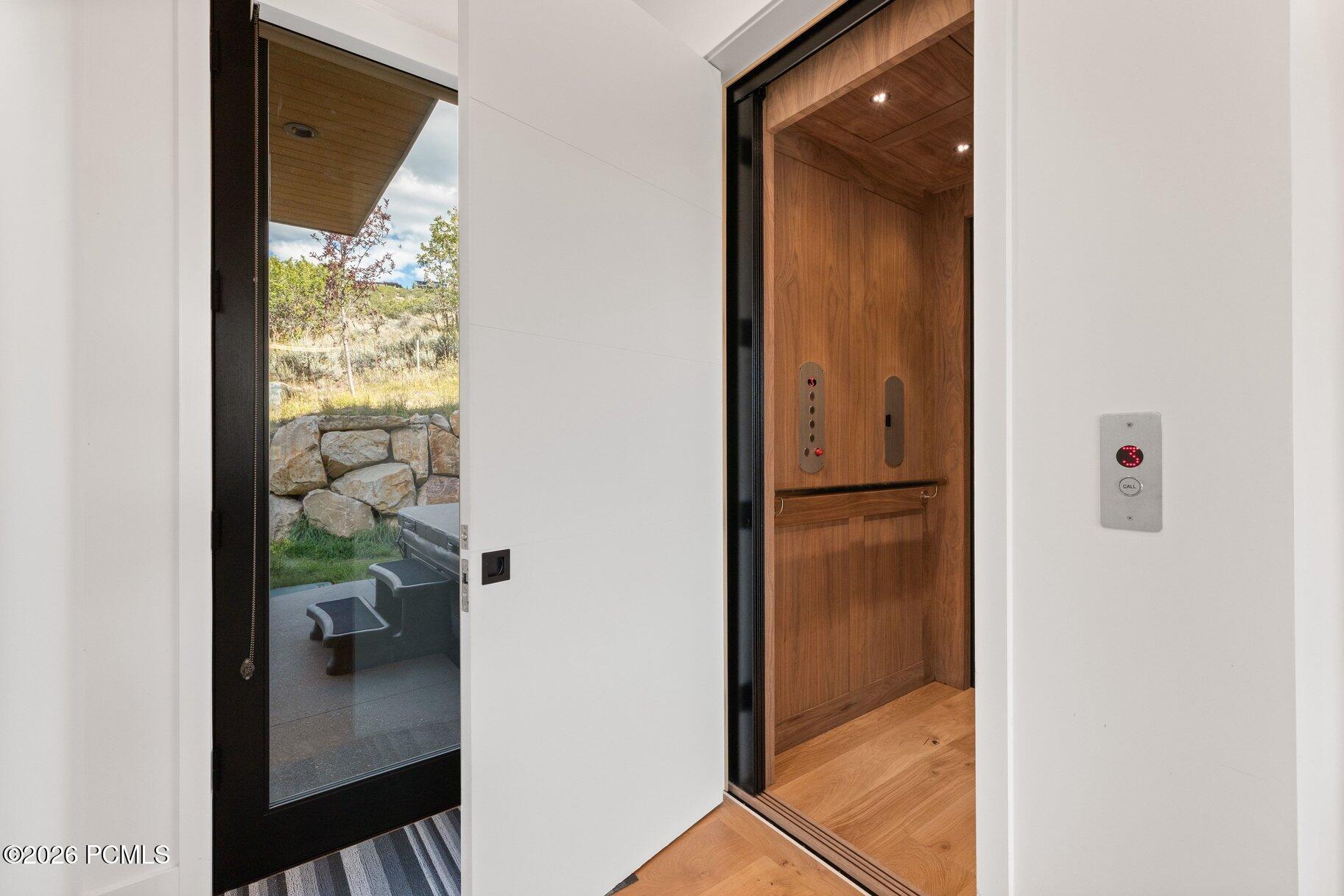 Open wood-paneled elevator beside a glass door overlooking stone landscaping and outdoor seating.