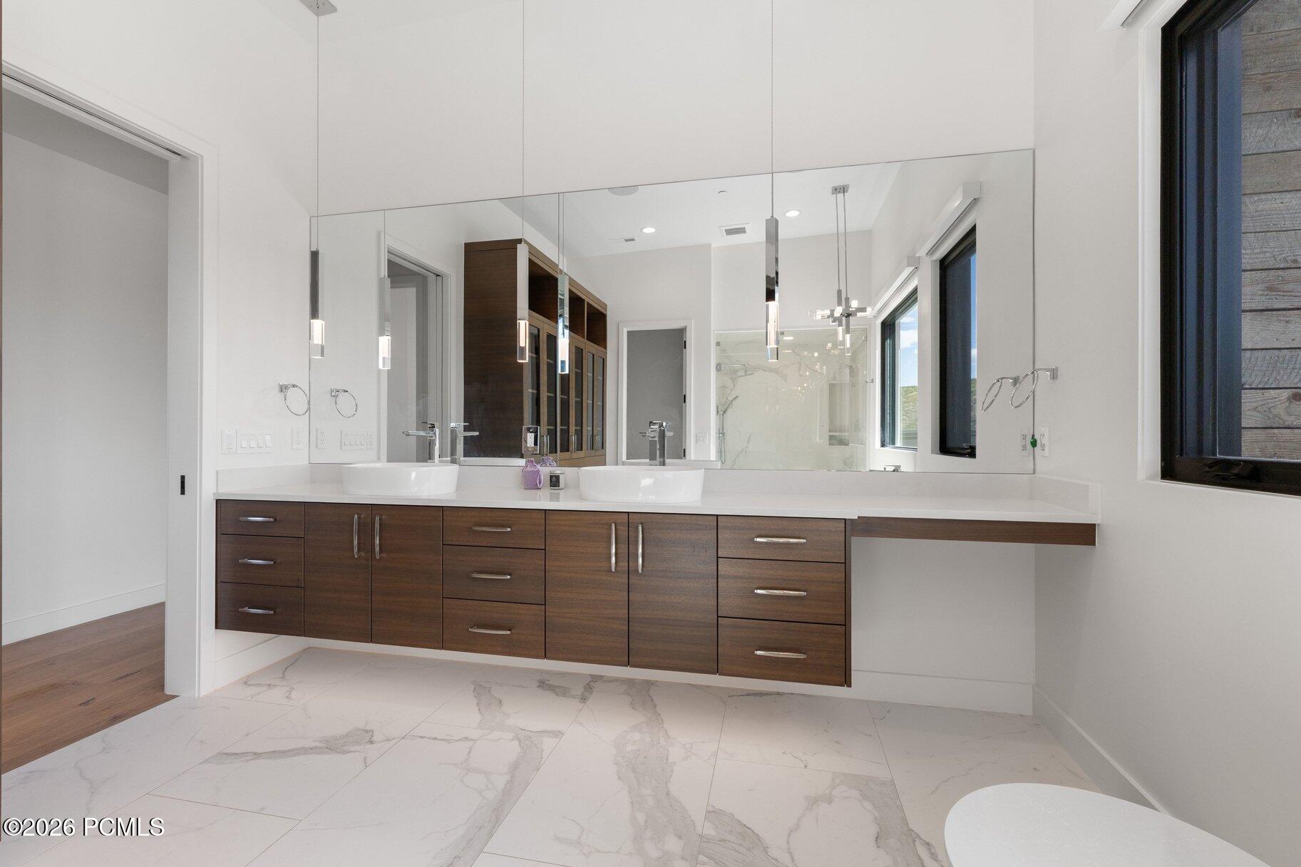 Modern bathroom with double vessel sinks, dark wood vanity cabinets, and marble-look tile flooring.