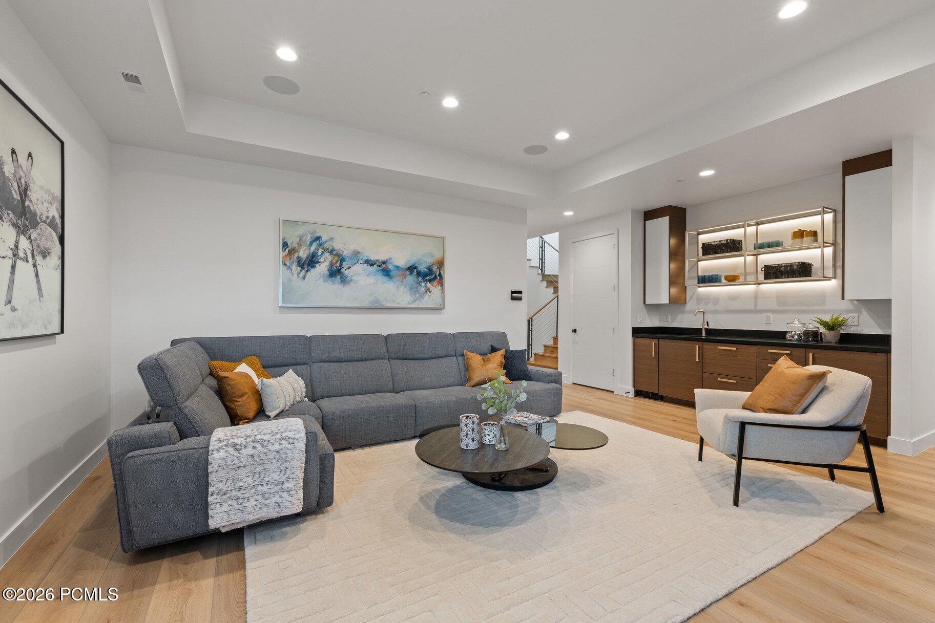 Living room with a gray sectional, pale rug, and built-in bar with illuminated shelves.