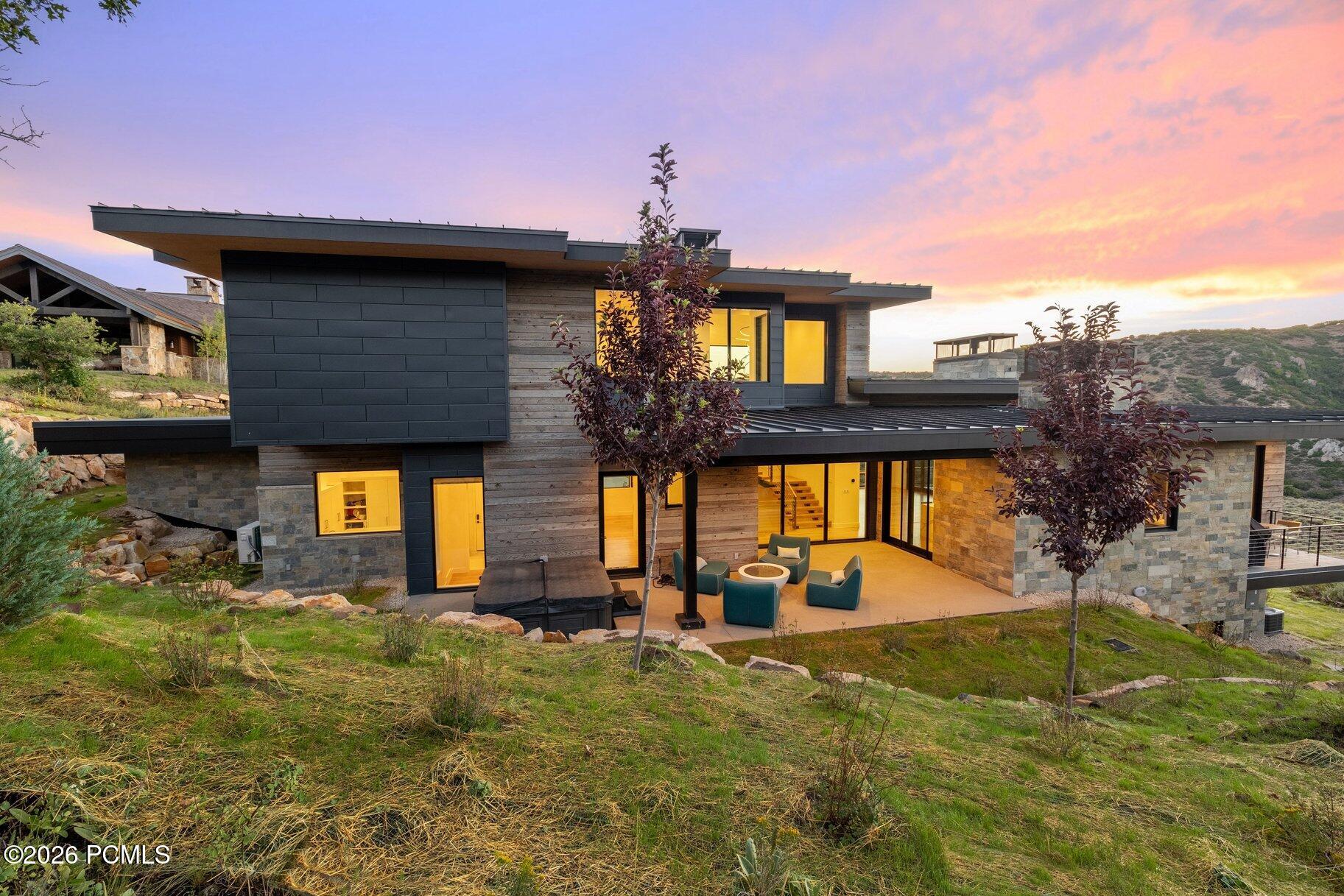 Modern Park City home with stone walls, broad windows, and a furnished patio at sunset.