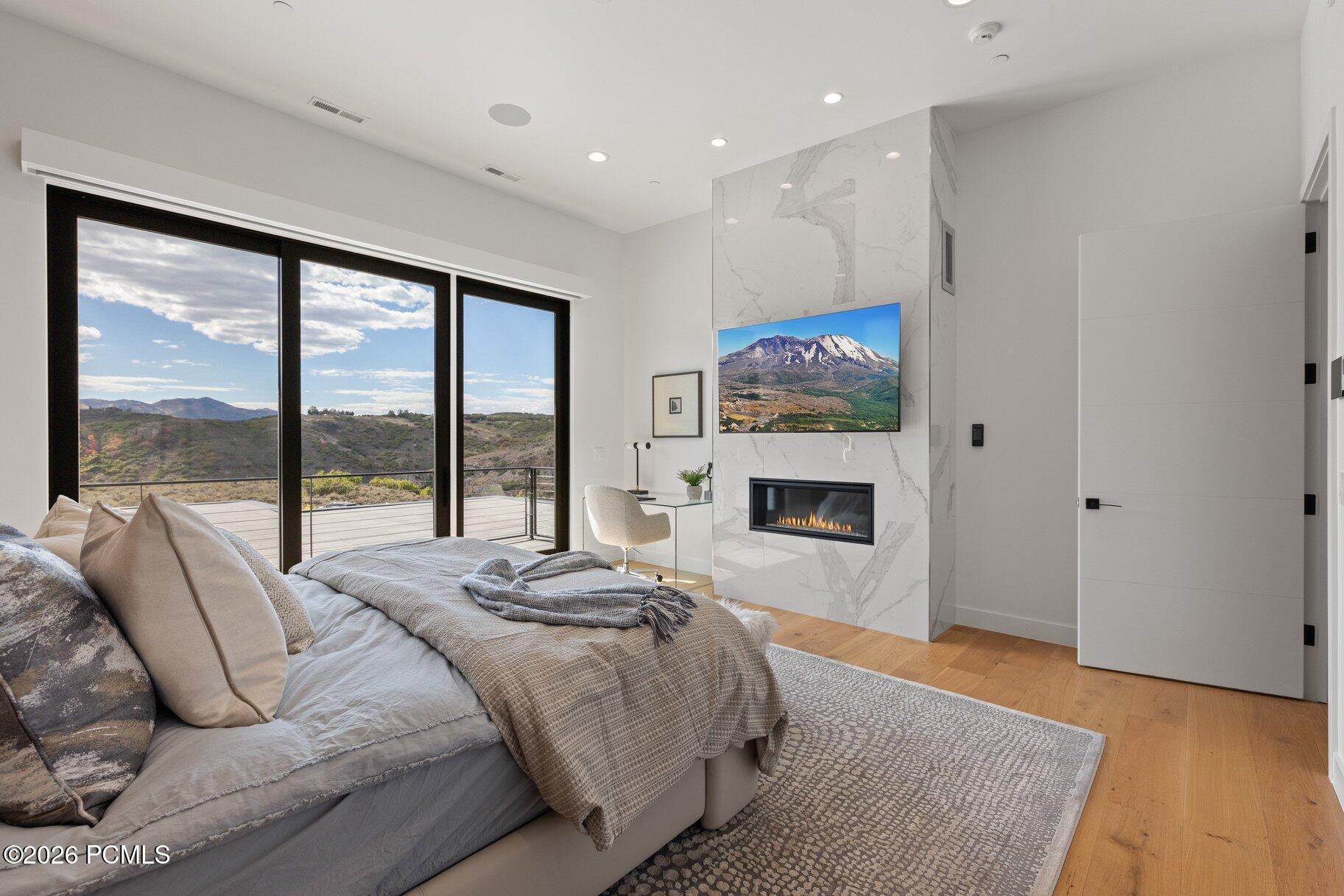 Modern bedroom with marble fireplace, floor-to-ceiling windows, and mountain views.