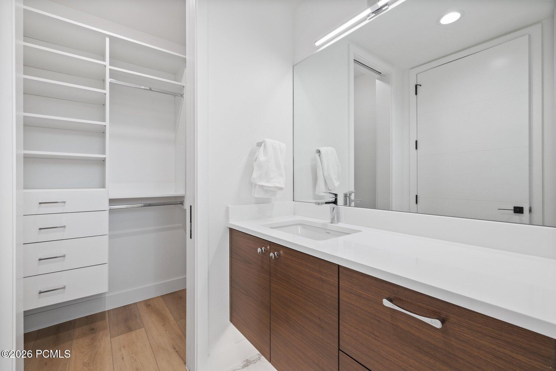 Modern bathroom vanity with a white countertop and dark wood cabinets beside an open walk-in closet.