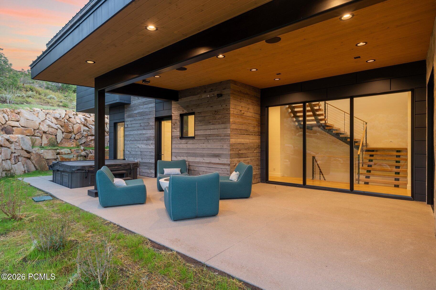 Modern home patio with blue lounge chairs, a hot tub, and glass doors showing an interior staircase.