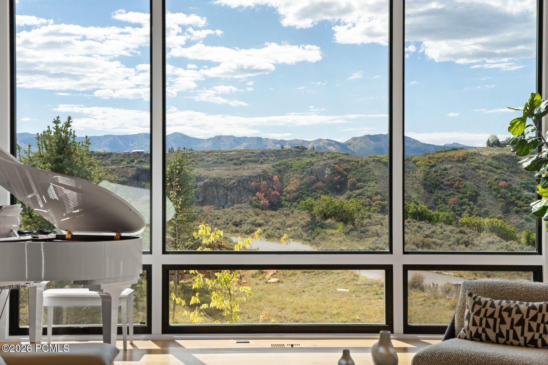 Living room with floor-to-ceiling windows framing a broad mountain view and white grand piano.