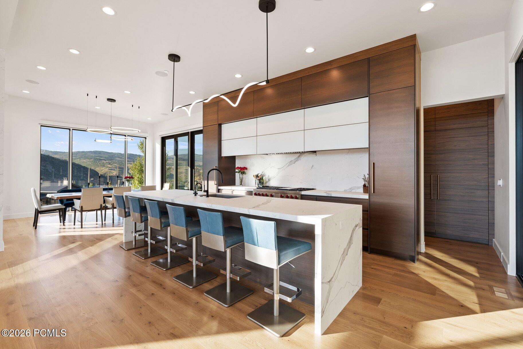 Modern kitchen with a marble island and blue stools, opening to mountain views.
