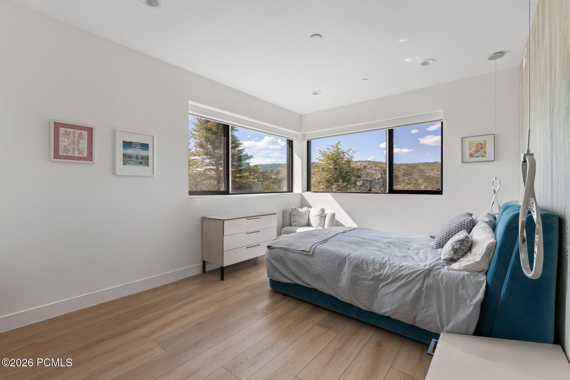 Bright bedroom with a teal bed and corner windows overlooking wooded hills.