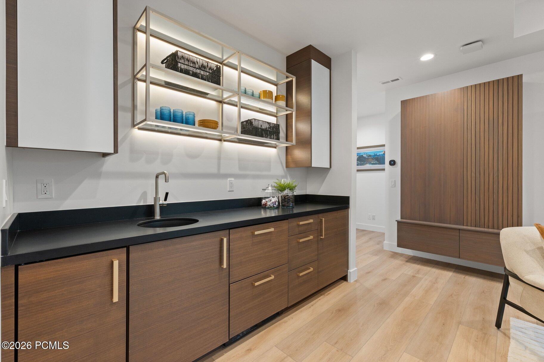 Modern kitchen with dark wood cabinetry, black counters, and illuminated open shelving.