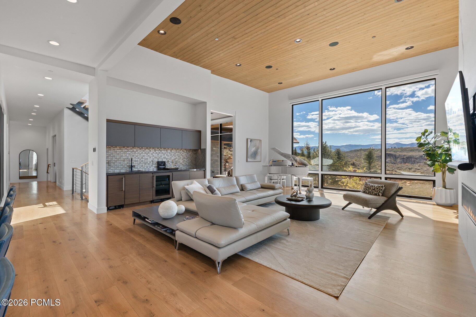 Modern living room with a wood-plank ceiling, white seating, and large windows overlooking the mountains.
