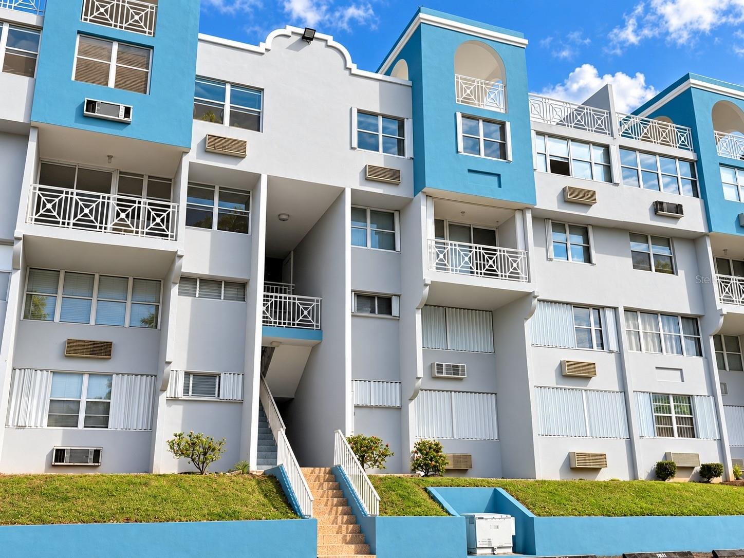 Blue-and-white apartment building with geometric balconies and a central exterior stairway.