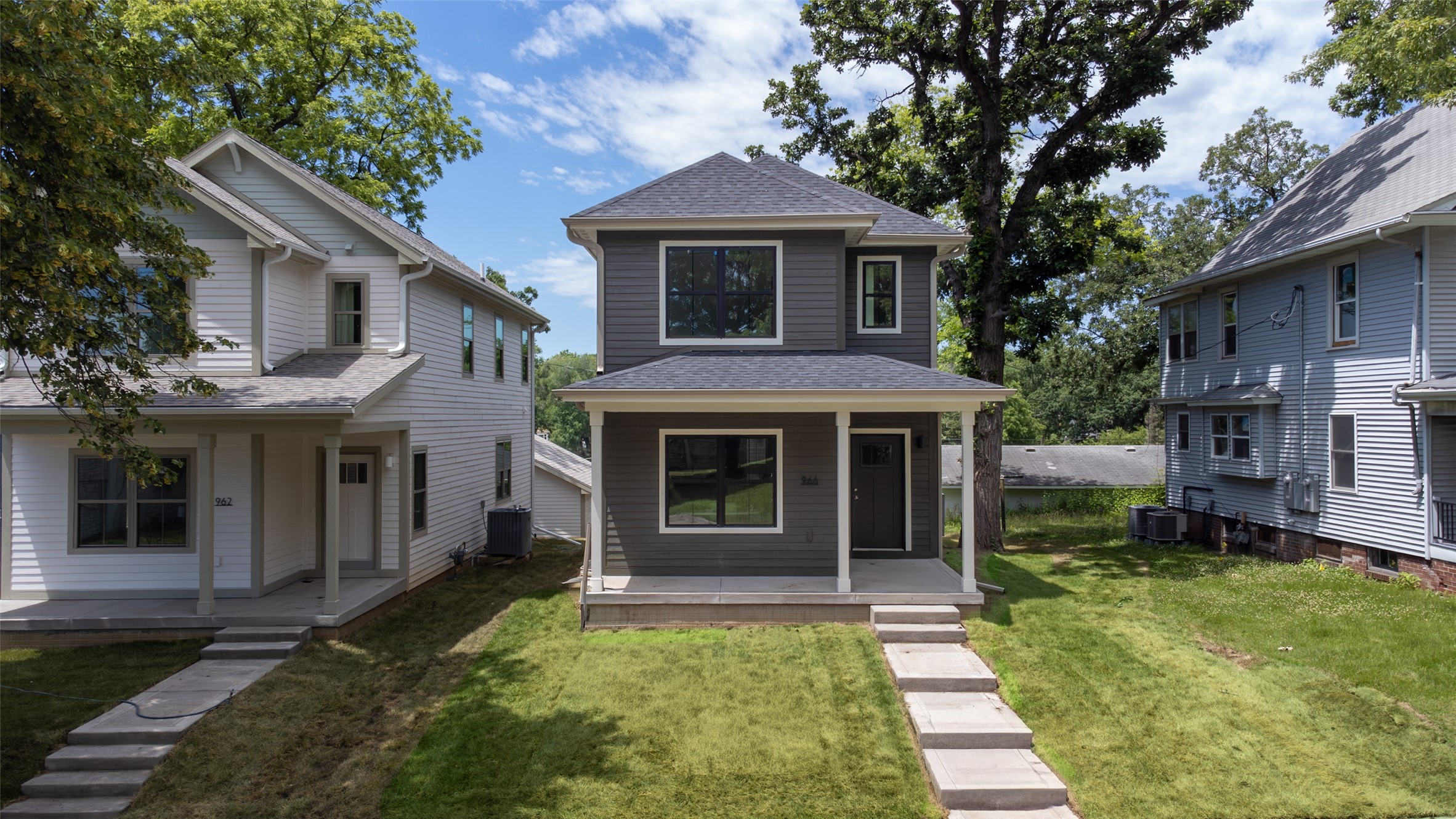 Two-story gray house with a covered porch, concrete walkway, and mature trees.