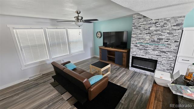 Living room with a brown leather sofa, stone fireplace wall, and large windows with blinds.
