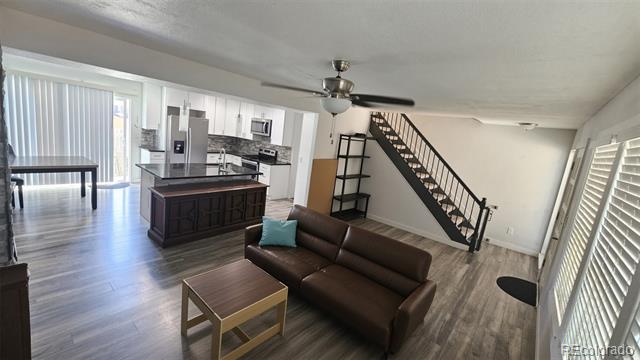 Open-plan living room and kitchen with a dark sofa, large island, and staircase with black railings.