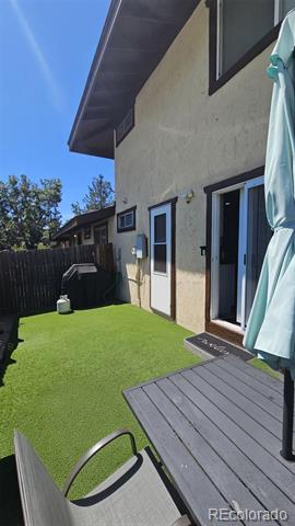 Backyard patio with artificial turf, a raised deck, and a fenced yard beside the house.