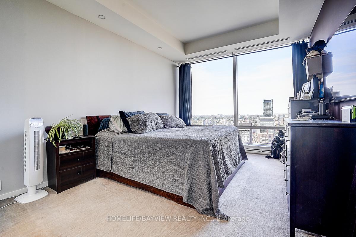 Furnished bedroom with a large bed and floor-to-ceiling windows overlooking the city skyline.