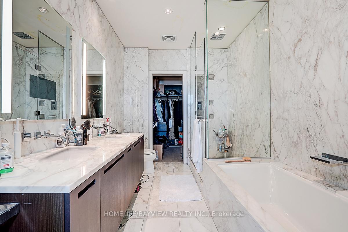 Marble ensuite bathroom with a long vanity, glass shower, large bathtub, and open closet.
