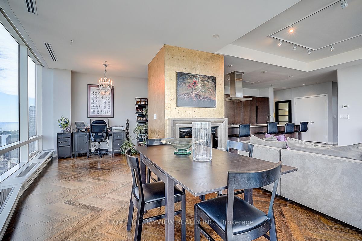 Open-concept penthouse dining and living area with a stone fireplace and floor-to-ceiling windows overlooking water and the city.