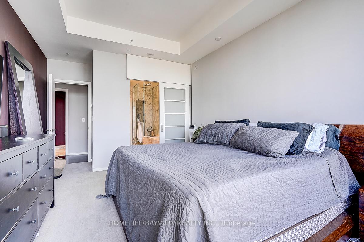 Bedroom with gray quilted bedding, dark wood headboard, and a glimpse of the marble-finished shower.