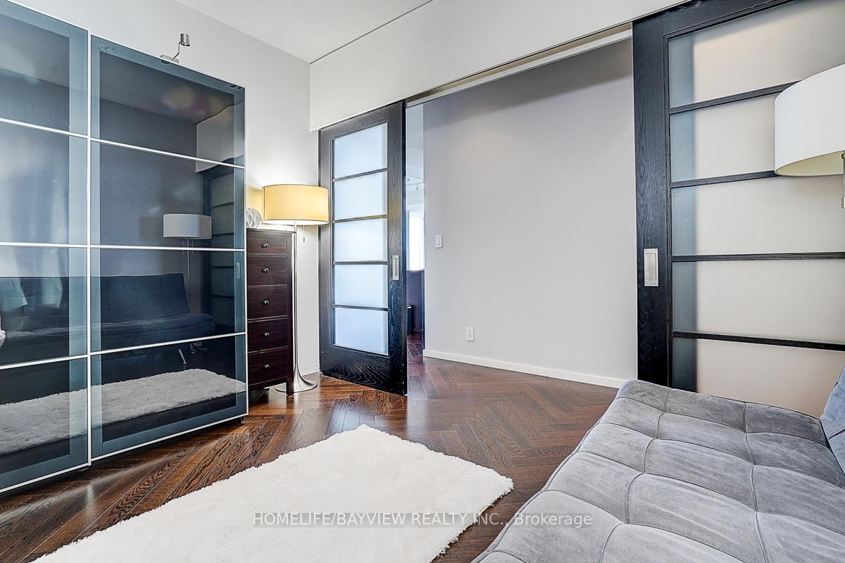 Condo living area with a gray sofa, sliding glass partitions, and herringbone wood floors.