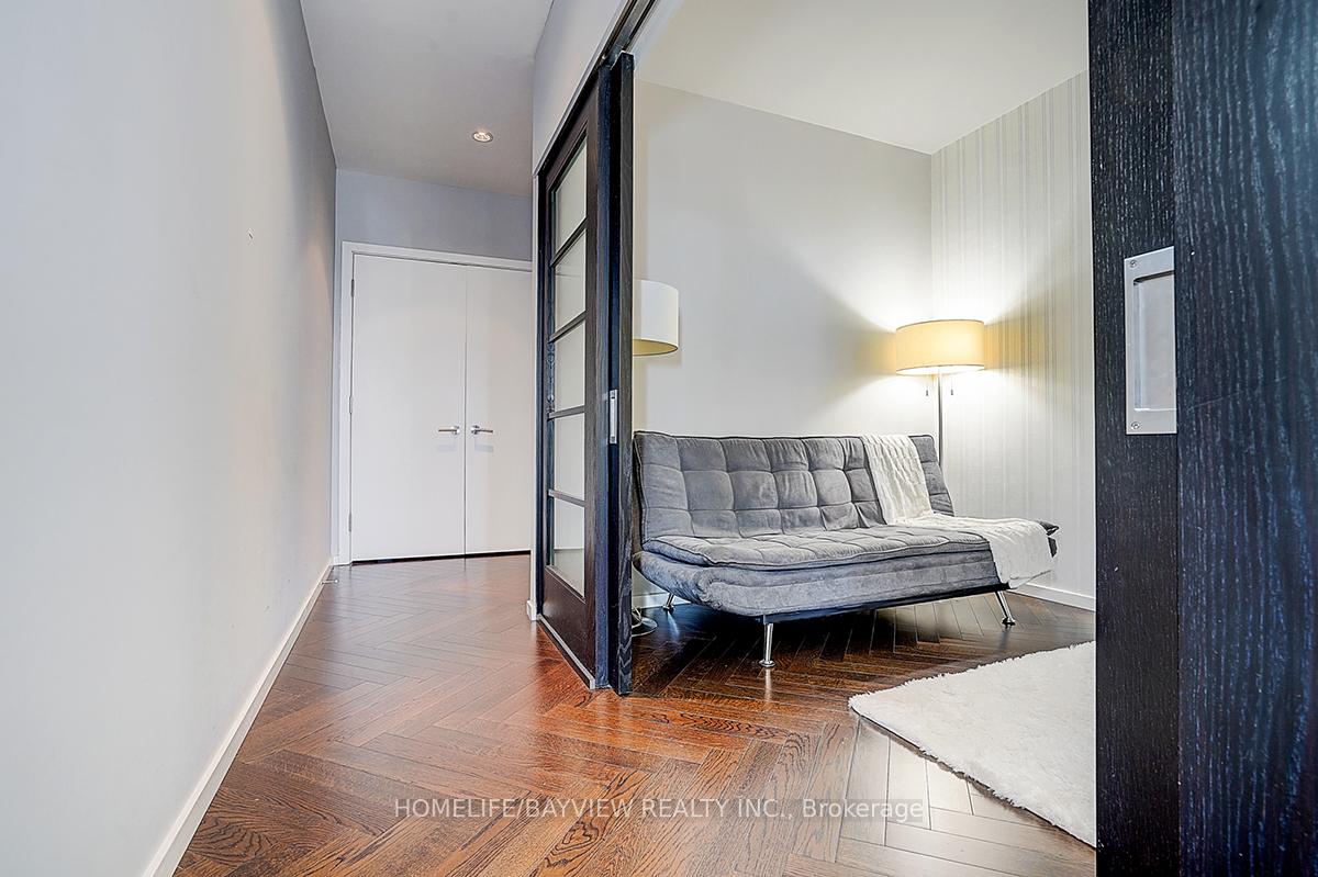 Furnished condo den with a gray tufted sofa, floor lamp, and dark wood flooring.