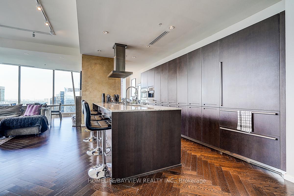 Modern condo kitchen with a large island, dark cabinetry, and floor-to-ceiling windows overlooking the city.
