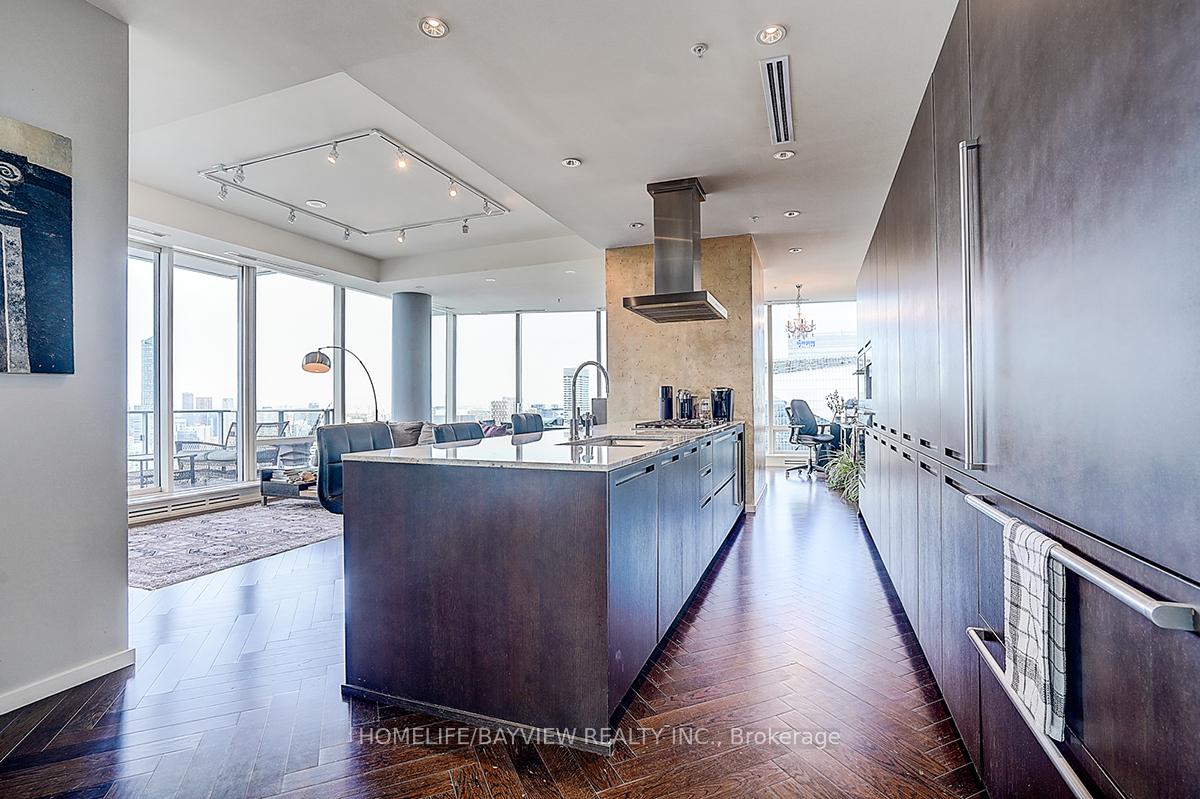 Modern condo kitchen with a large dark island and floor-to-ceiling windows overlooking the city.