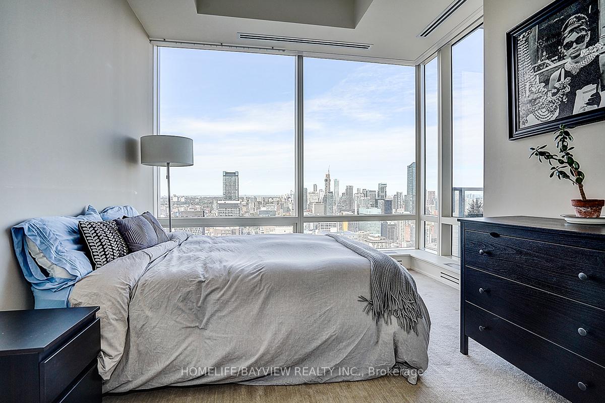 Furnished high-rise bedroom with a large bed and floor-to-ceiling windows overlooking the Toronto skyline.