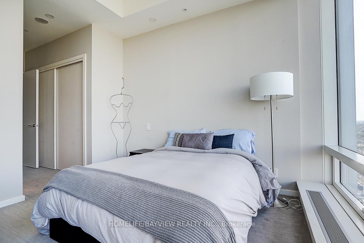 Furnished condo bedroom with a large bed beside floor-to-ceiling windows overlooking the city.
