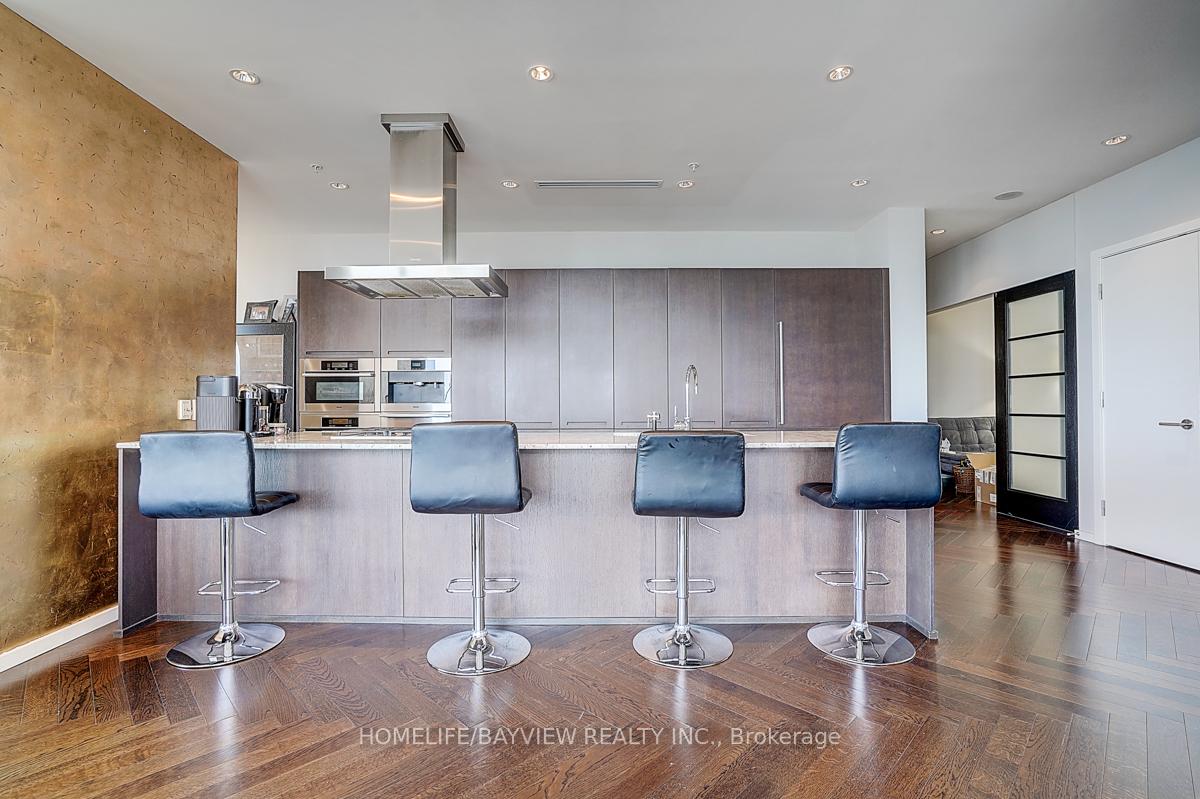 Modern condo kitchen with a large island, four blue bar stools, and a gold-toned accent wall.