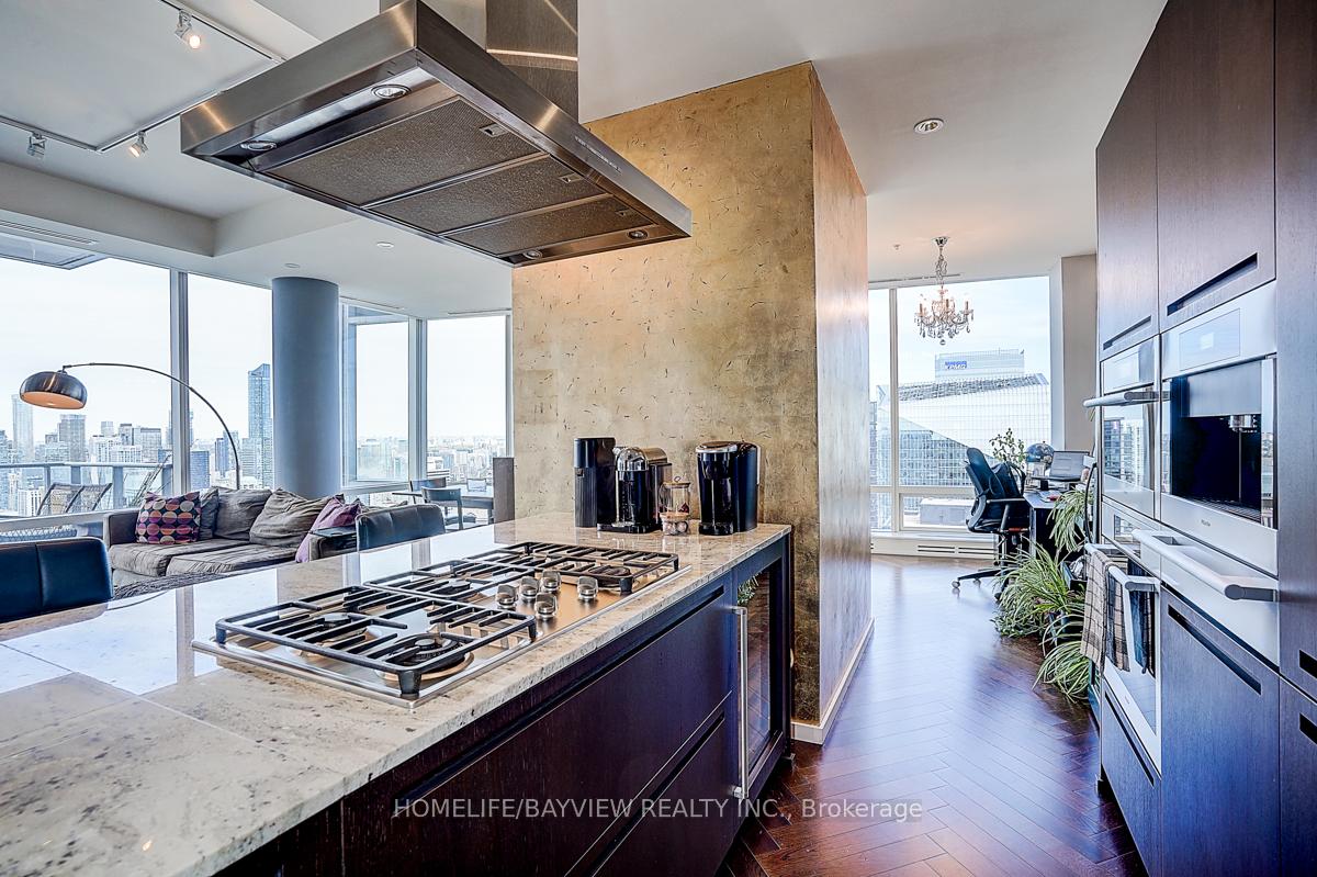 Modern condominium kitchen with a marble island, gas cooktop, dark cabinetry, and Toronto skyline views.
