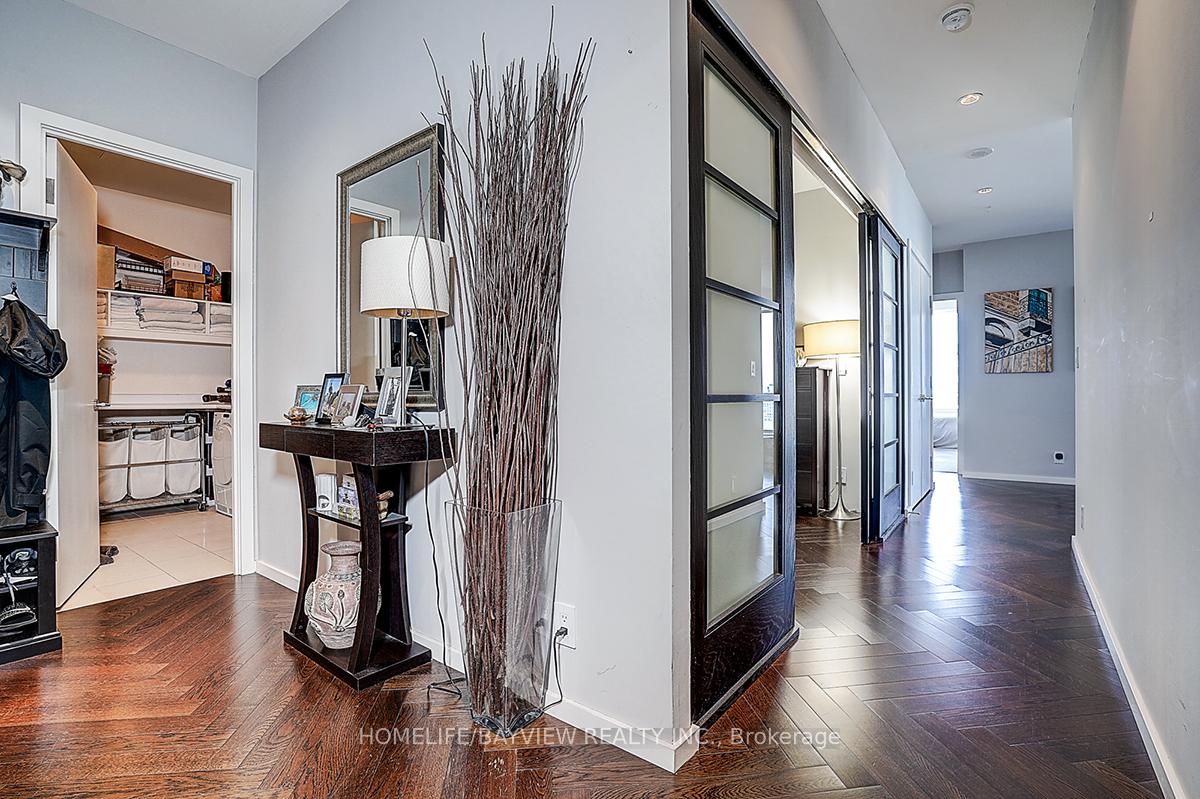 Condo foyer with herringbone wood floors, console table, mirror, and black-framed glass doors.