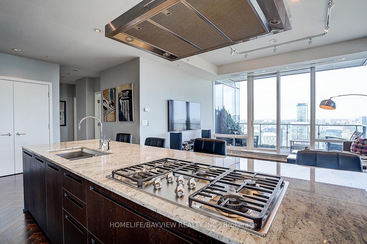 Penthouse kitchen with a large stone island, gas cooktop, and floor-to-ceiling city-view windows.