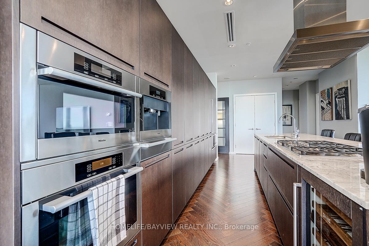 Modern condo kitchen with dark cabinetry, a stone island, gas cooktop, and stainless steel Miele ovens.
