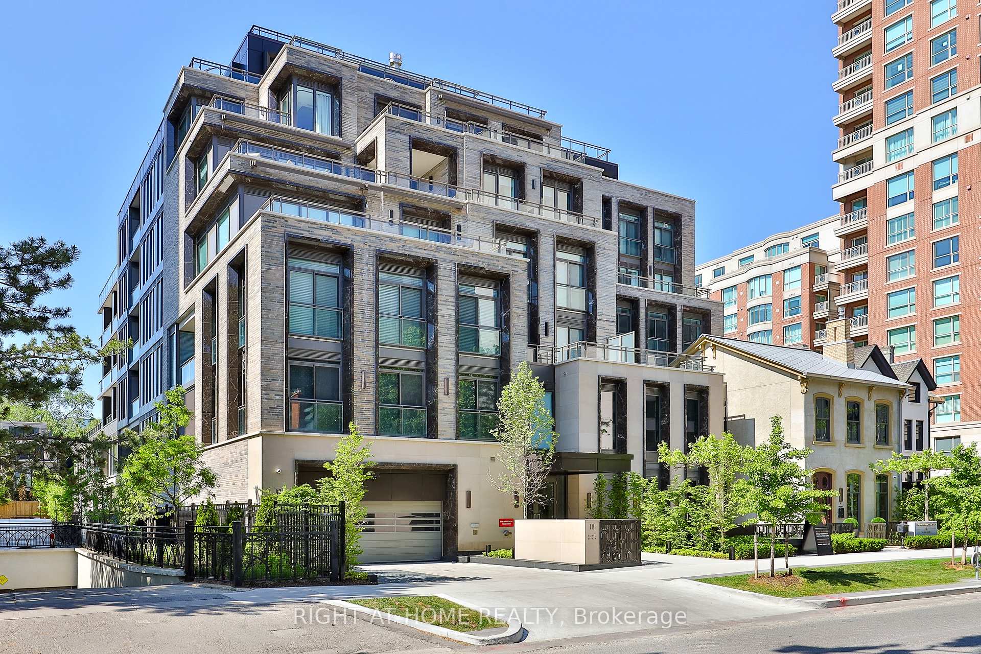 Modern stone-clad condominium with glass balconies, landscaped frontage and driveway entrance.
