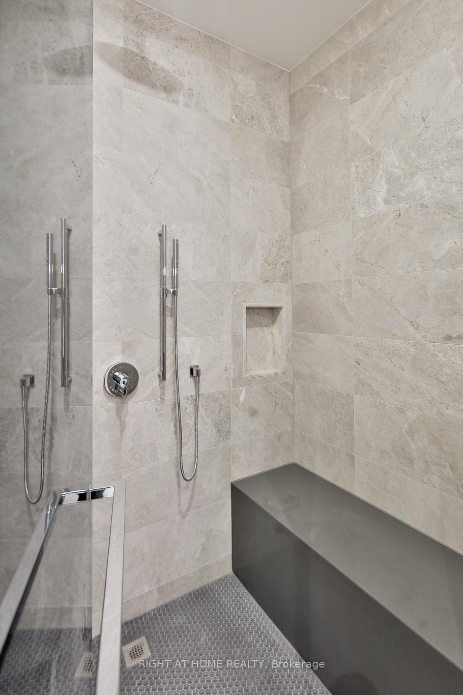 Walk-in shower with pale stone tiles, a dark built-in bench, and handheld shower fixtures.