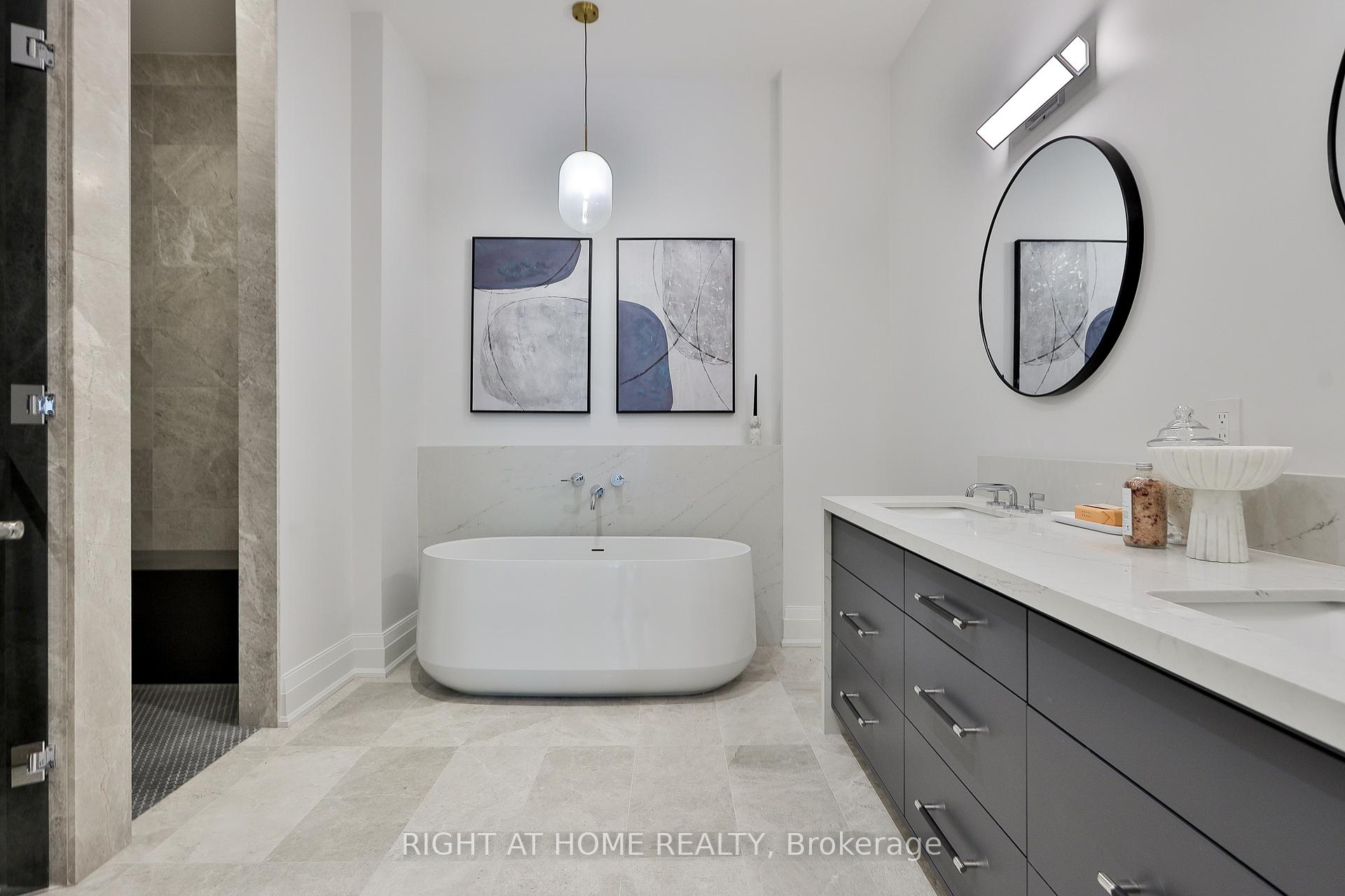 Modern bathroom with a freestanding soaking tub, dark double vanity, and stone-tiled shower.