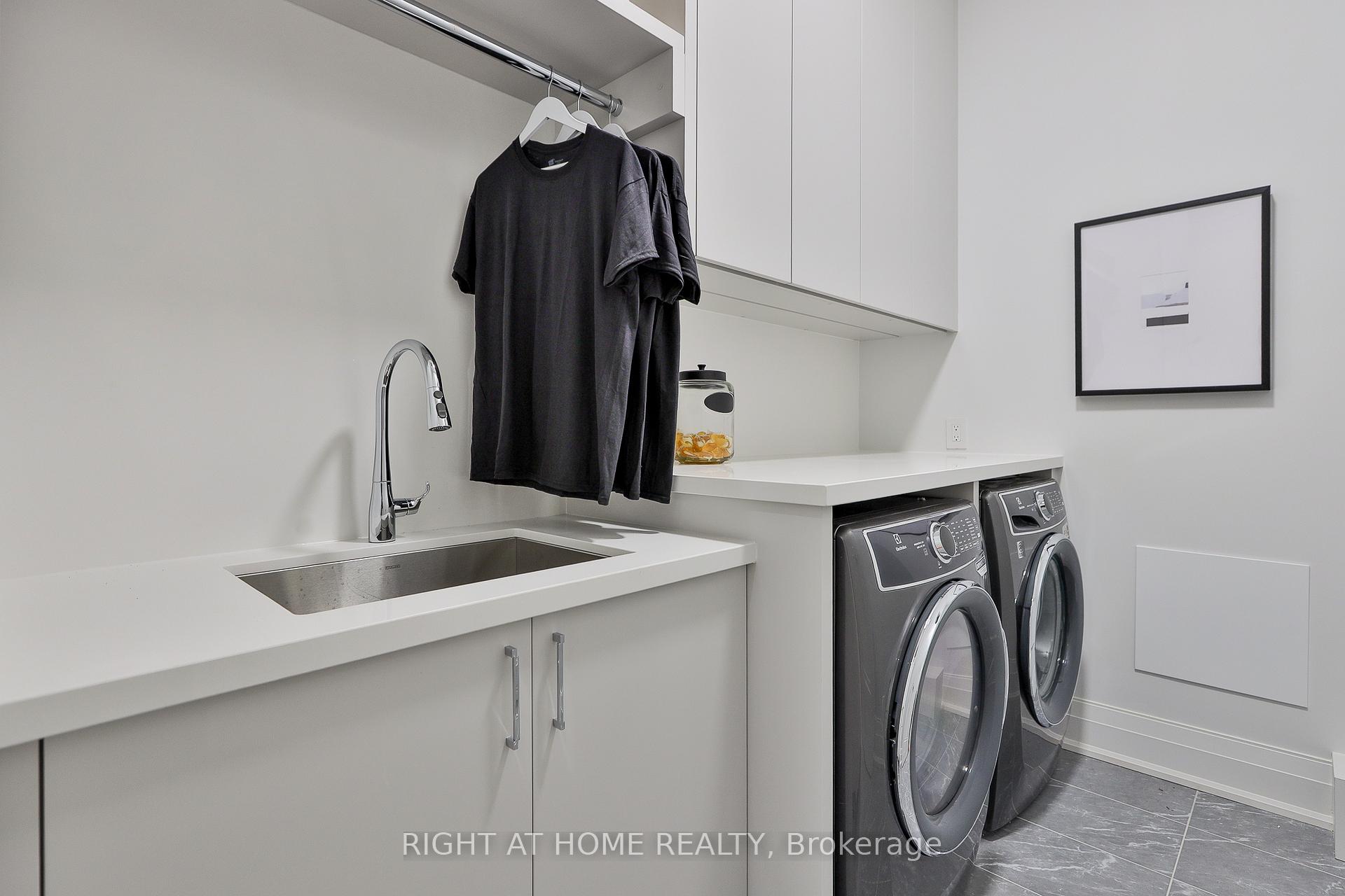 Modern laundry room with a utility sink, front-loading washer and dryer, and shirts hanging above the counter.