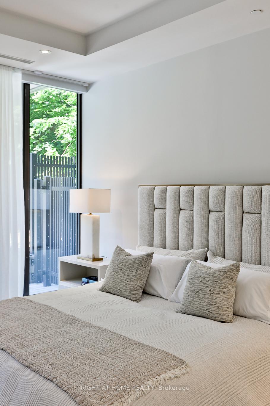 Furnished bedroom with a tall upholstered headboard and glass door overlooking leafy greenery.