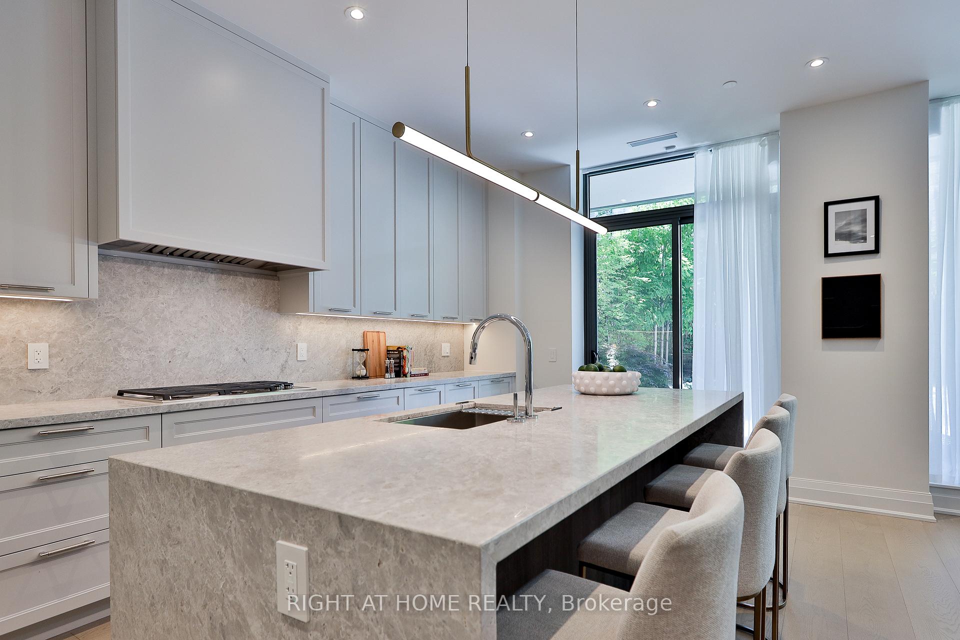 Modern kitchen with a large stone island, gray cabinetry, and glass doors overlooking greenery.