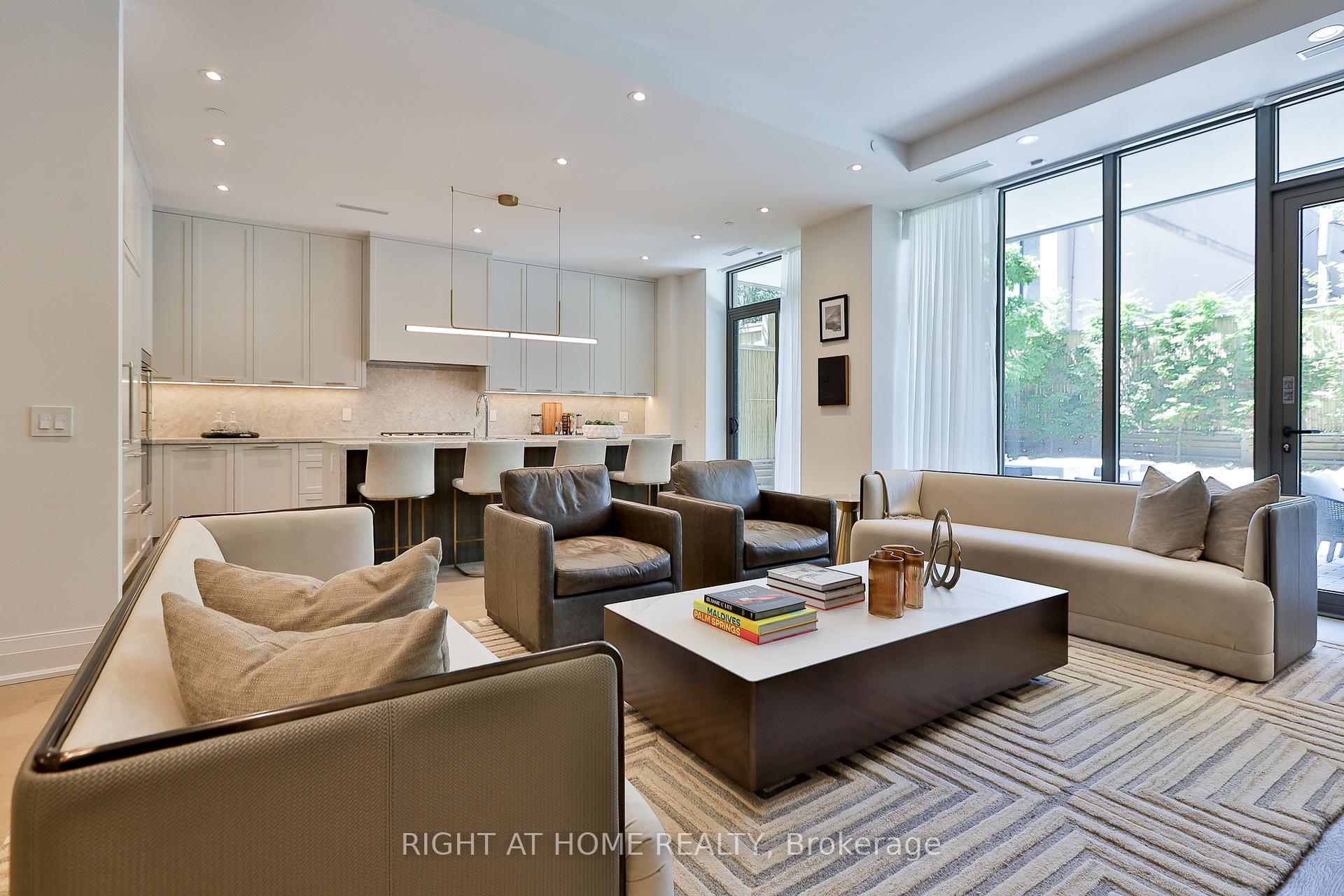 Open-plan living room and kitchen with neutral seating, white cabinetry, and floor-to-ceiling windows facing a garden patio.