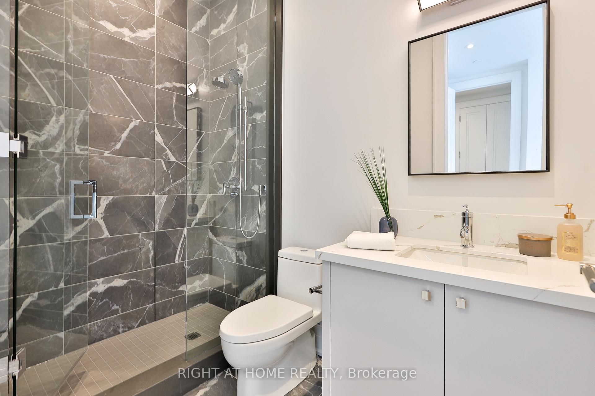 Modern bathroom with a marble-look glass shower, white vanity, large mirror, and toilet.