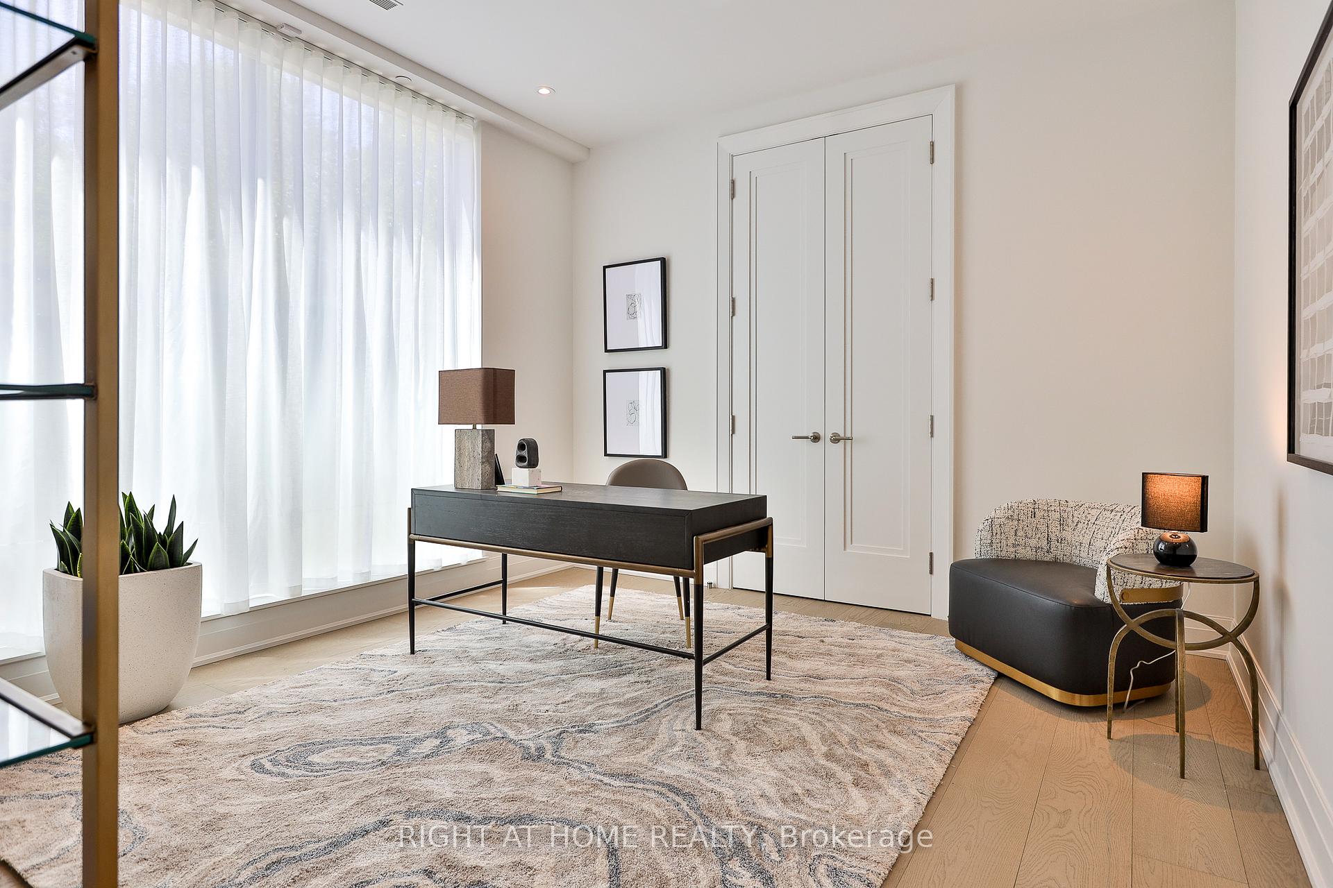 Staged home office with a dark desk, tall curtained windows, and a patterned lounge chair.
