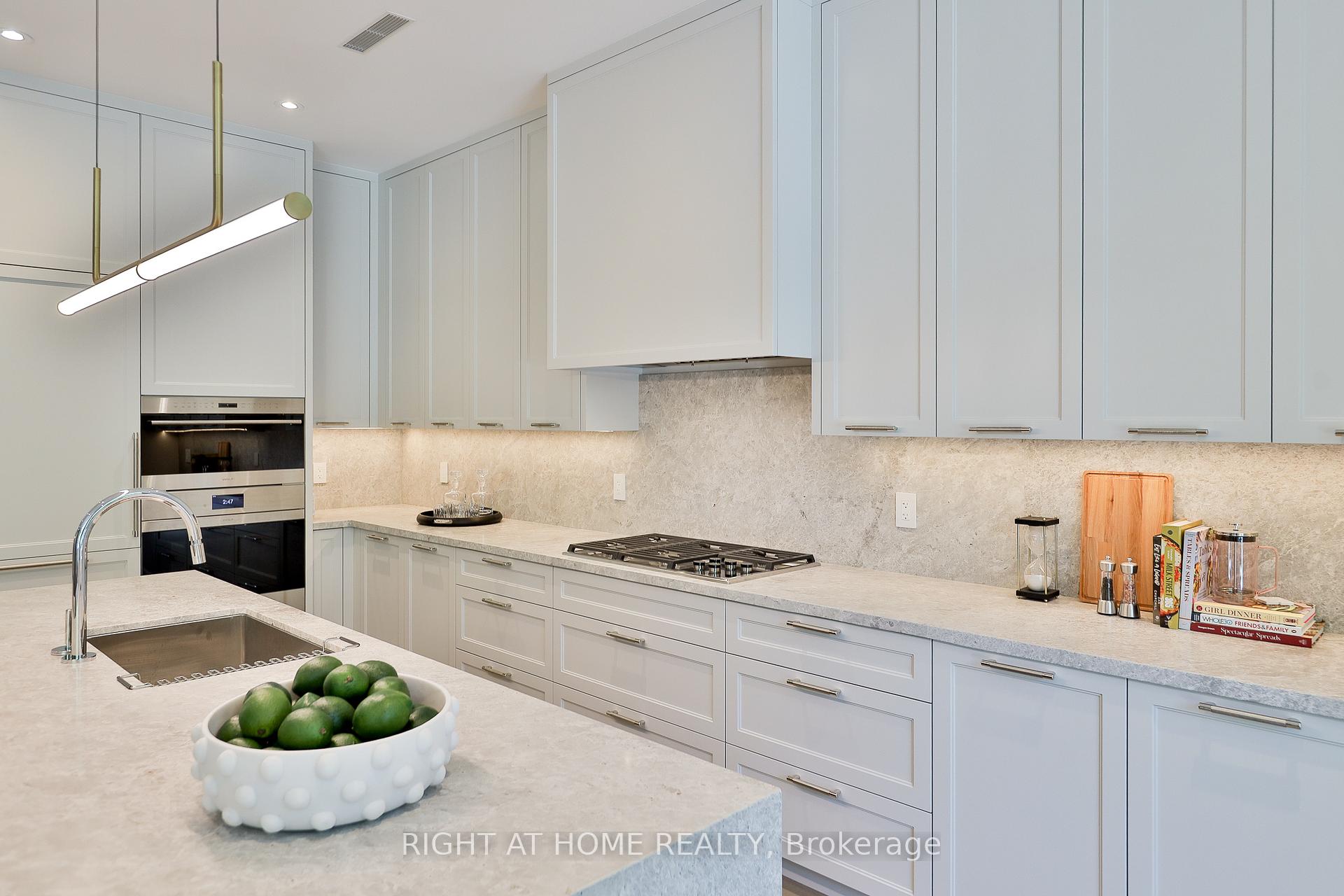 Modern kitchen with pale cabinetry, stone counters, a large island, and built-in double ovens.