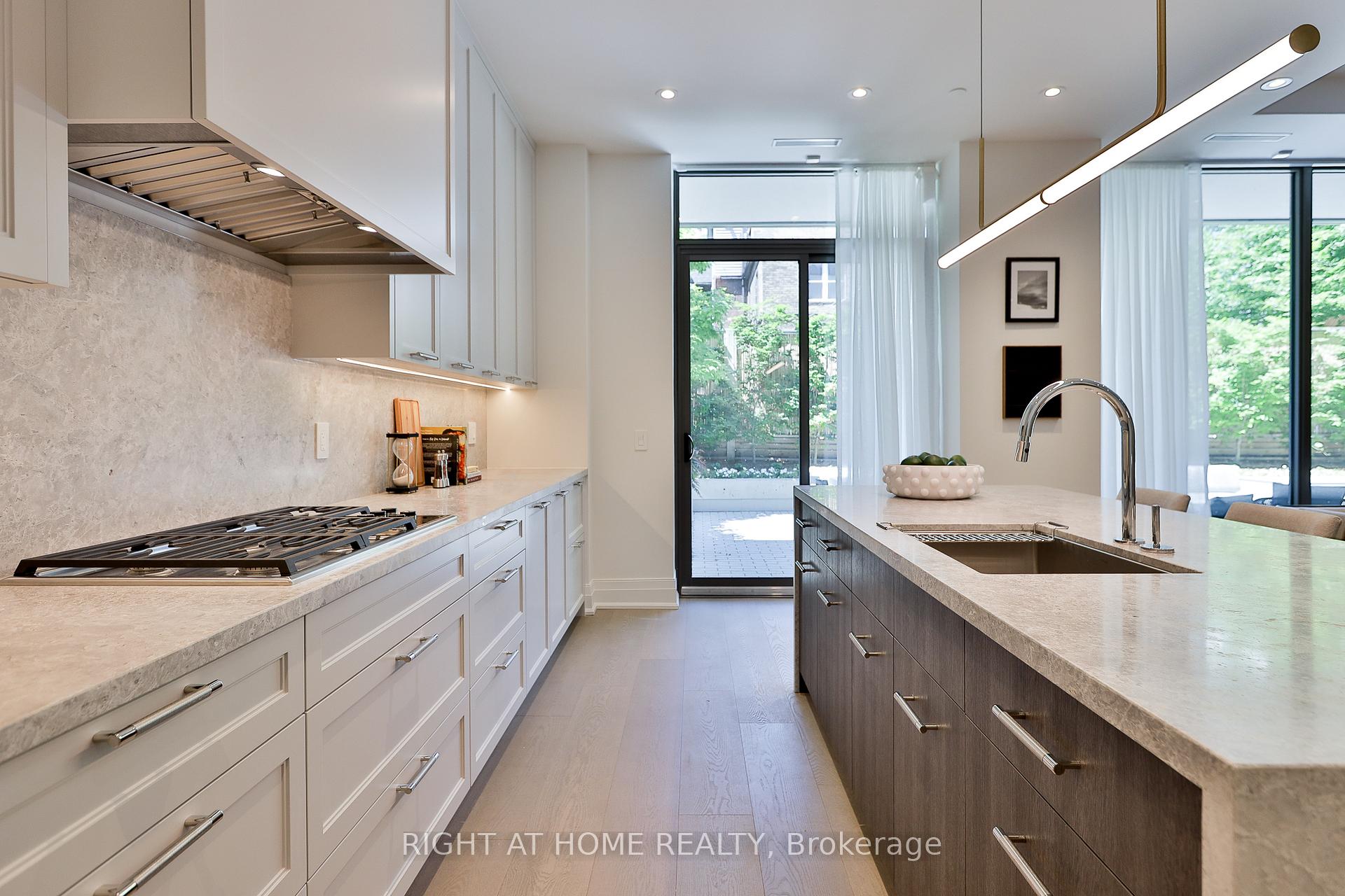 Modern kitchen with a dark wood island and sink, opening through sliding doors to a leafy patio.