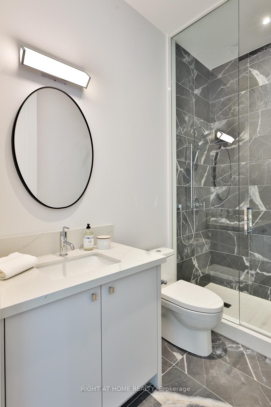 Modern bathroom with a white vanity, oval mirror, and glass shower lined with veined gray tile.