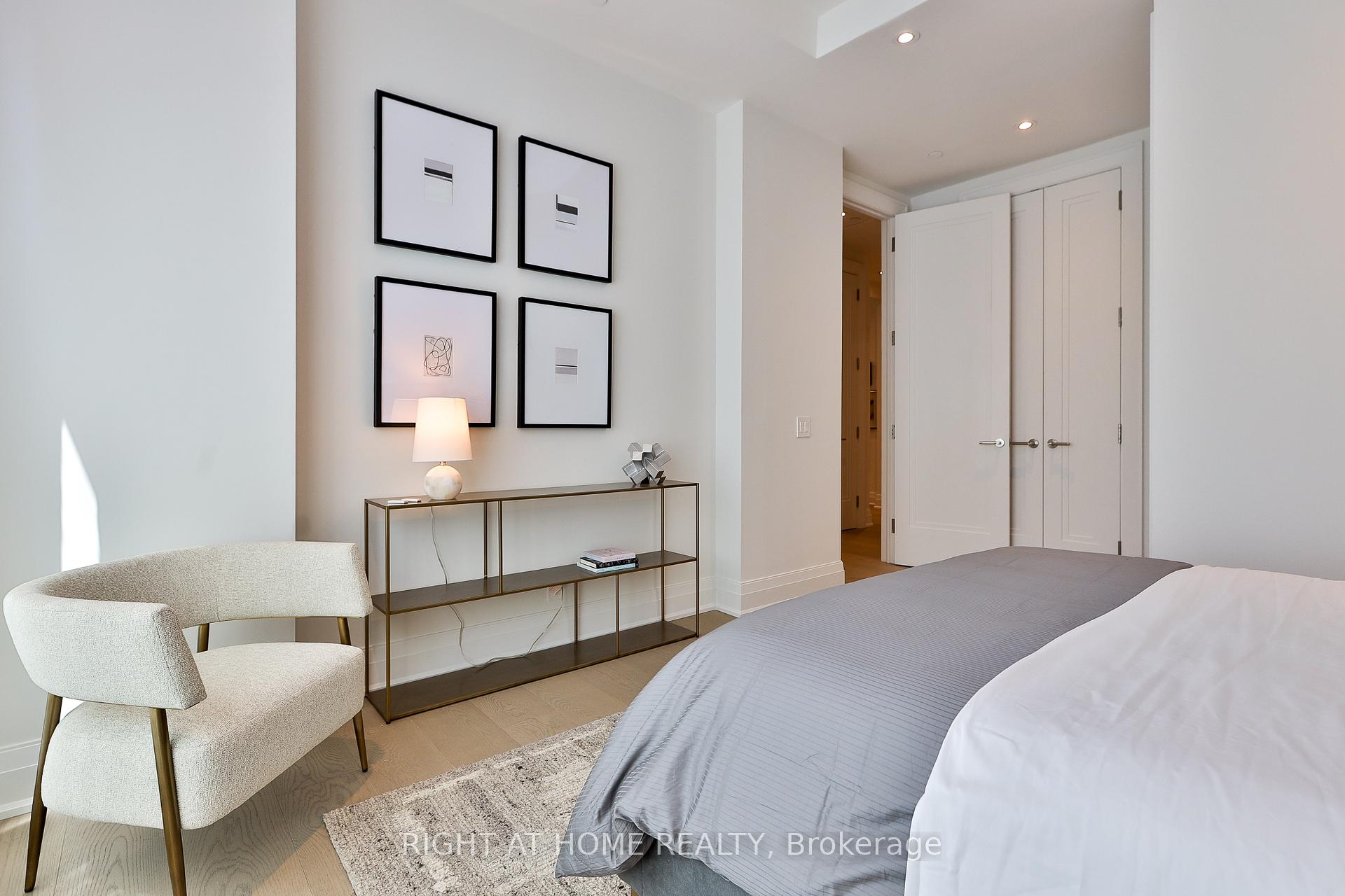 Staged bedroom with a gray bed, cream chair, framed prints, and slim console table.