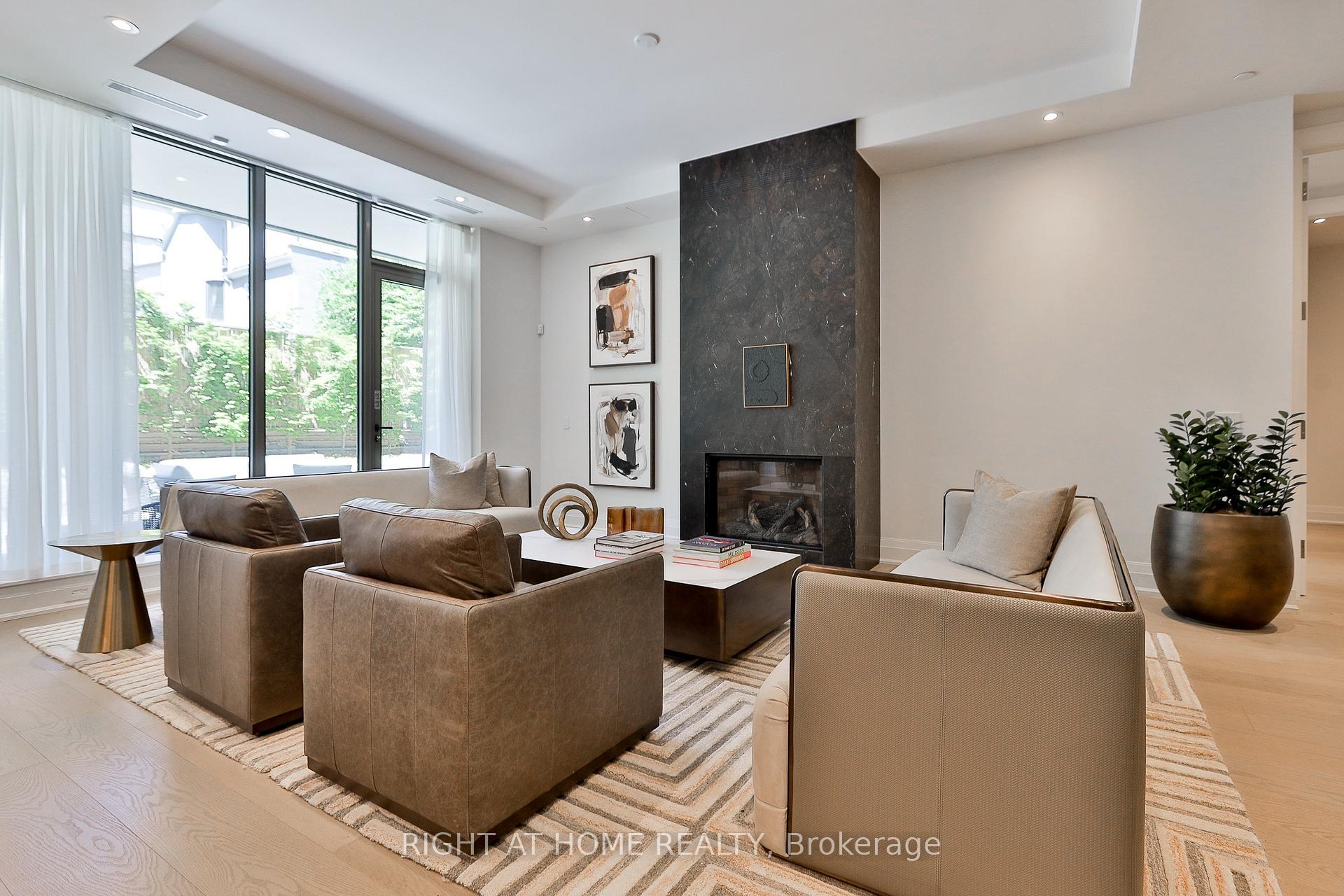 Living room with a dark stone fireplace, leather seating, and large windows overlooking greenery.