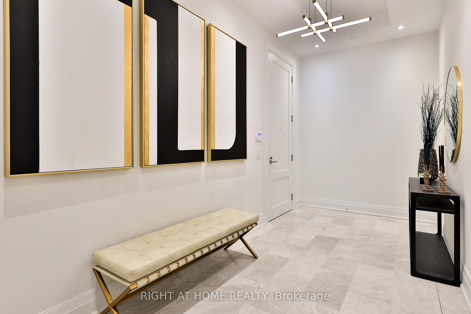 Entry hall with pale stone tile, a cream bench, black-and-gold artwork, and a geometric chandelier.