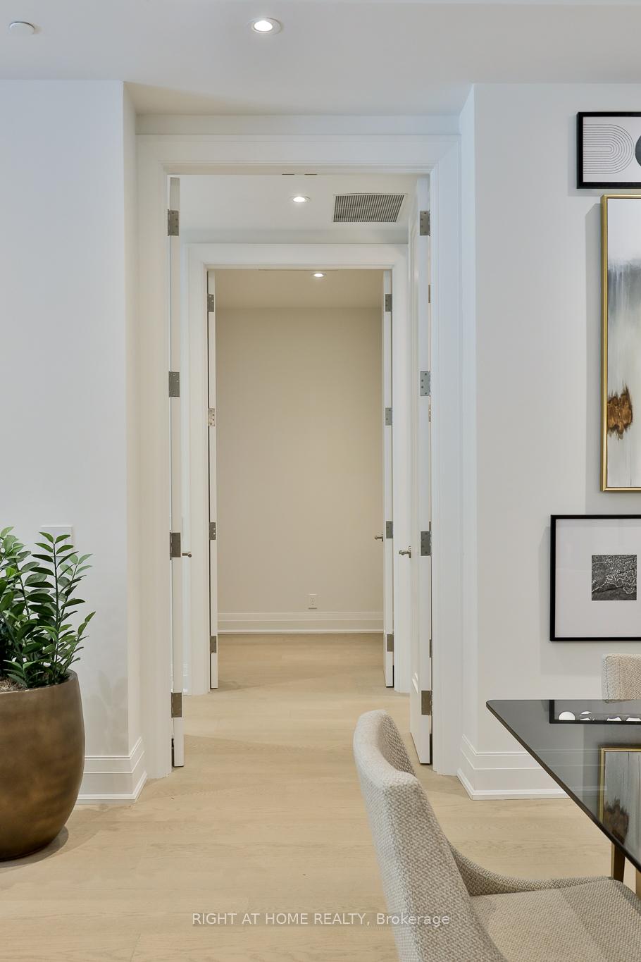 Bright hallway with pale hardwood floors, open doorways, framed art, and a potted plant.