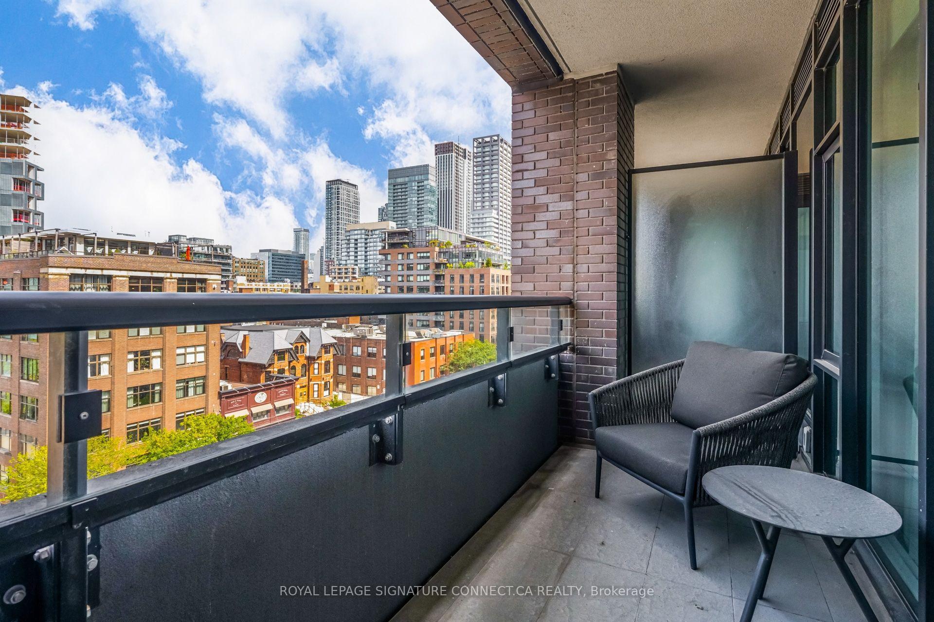 Condominium balcony overlooking downtown Toronto, furnished with a wicker chair and round table.